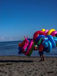 Multi colored balloons on beach against blue sky