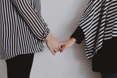 Midsection of couple holding hands against wall