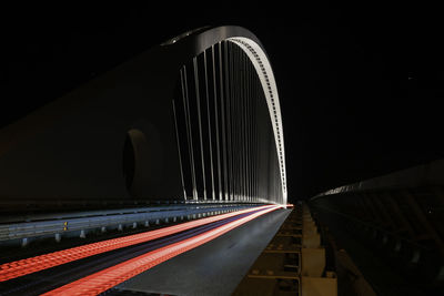 Light trails on bridge in city against sky at night