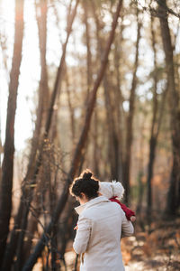Rear view of mother carrying baby girl standing against trees at forest