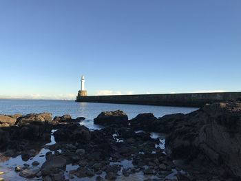 Lighthouse by sea against clear sky