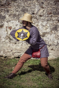 Rear view of boy holding ball on field against wall