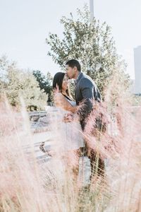 Young couple standing by tree against sky