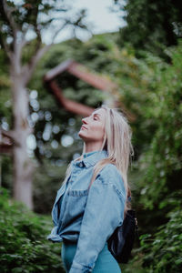 Side view of woman standing against trees facing up