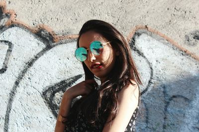 Young woman with long hair biting lips against graffiti wall