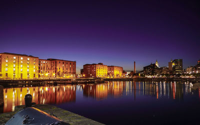 Illuminated buildings by river against sky at night