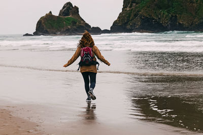 Woman traveler on oregon pacific coast at rainy day. running on the beach, windy weather