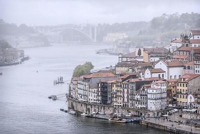 Bridge over river by buildings in city against sky