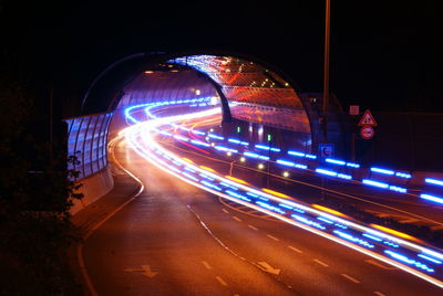 Light trails on street by tunnel at night
