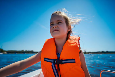 Cute girl wearing life jacket sitting against clear blue sky