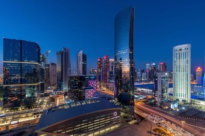 Illuminated modern buildings in city against clear blue sky