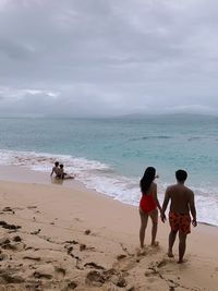 High angle view of couple holding hands while standing on shore at beach against sky