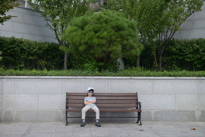 Boy sitting on bench against trees