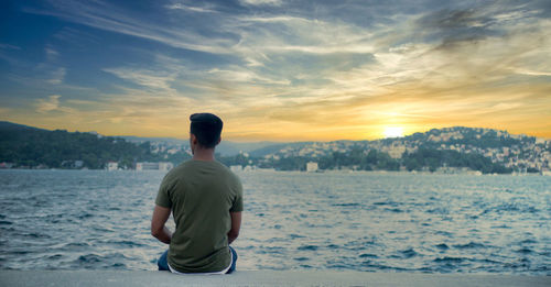 Rear view of man looking at sea against sky during sunset