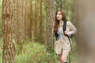 Young woman standing against tree trunk