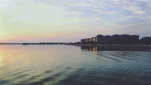 Scenic view of sea by buildings against sky during sunset