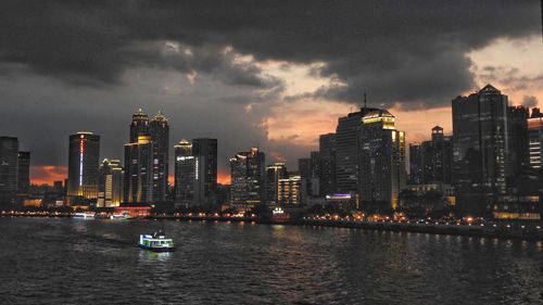 Scenic view of river by buildings against sky during sunset
