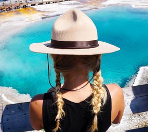 Rear view of woman wearing hat while sitting against lake