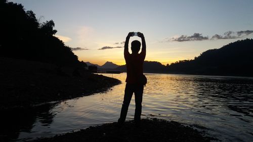 Silhouette man standing by lake against sky during sunset