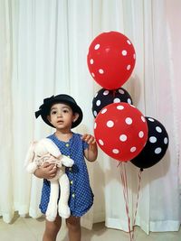 Girl holding balloons while standing by curtain at home