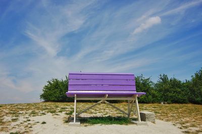 Empty bench on beach against sky