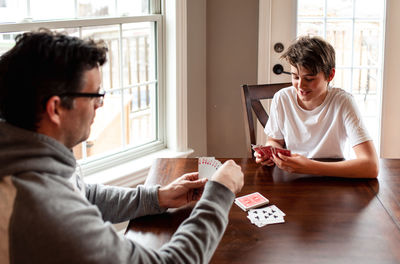 Adolescent boy and his father playing cards at the table together.