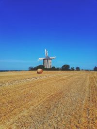 Windmill on field against clear blue sky