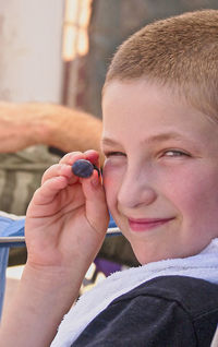 Close-up portrait of smiling boy holding blueberry