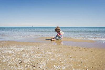 Rear view of woman standing at beach against clear sky