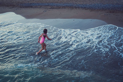 Girl in swimsuir run across the waves