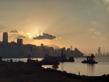 Silhouette buildings by sea against sky during sunset