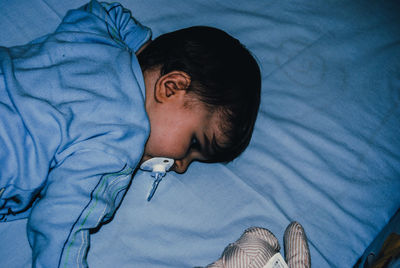 Cute boy sucking pacifier on bed at home