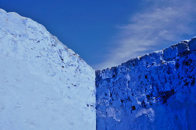 Low angle view of snow covered mountain against blue sky