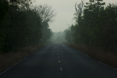 Empty road amidst trees against sky