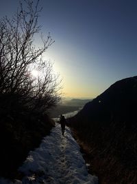 Silhouette person on street during winter against sky at sunset