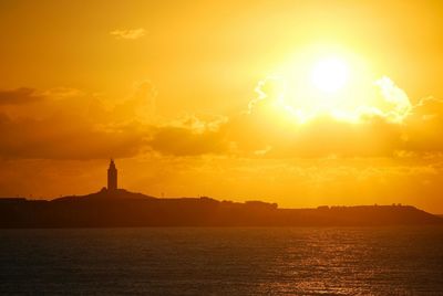 Silhouette lighthouse by sea against sky during sunset