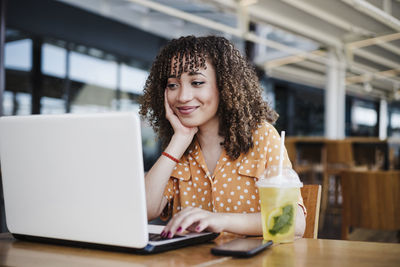 Portrait of young woman using phone while sitting on table