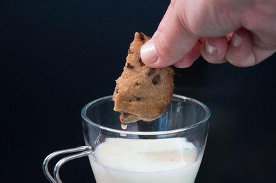 Close-up of hand holding chocolate cookie over milk with black background