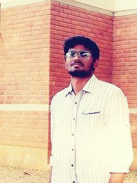 Portrait of young man standing against brick wall