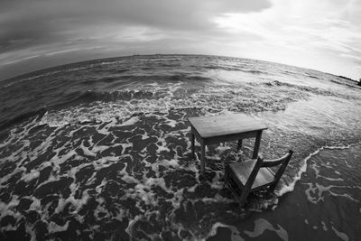 Empty table and chair on sea against cloudy sky