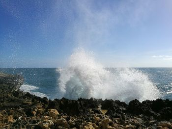 Waves splashing on rocks at shore against sky