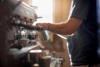 Midsection of man pouring coffee in cafe