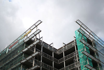 Low angle view of crane by building against sky