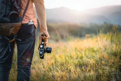 Person holding film camera on mountain meadow at sunset