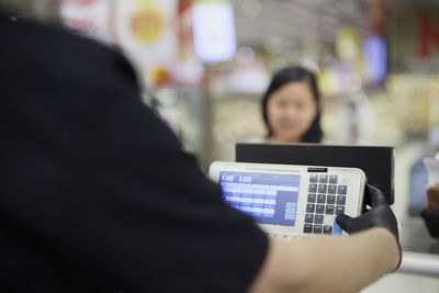 Shop assistant using scale at deli counter, female customer in background