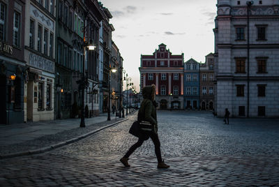 Side view of man walking by buildings in city