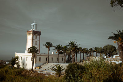 Lighthouse amidst trees and buildings against sky