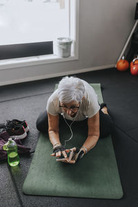 Senior woman using phone while stretching on mat in gym