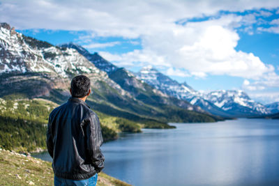 Rear view of man standing by lake against mountains