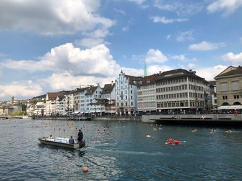 Boats in river by buildings in city against sky